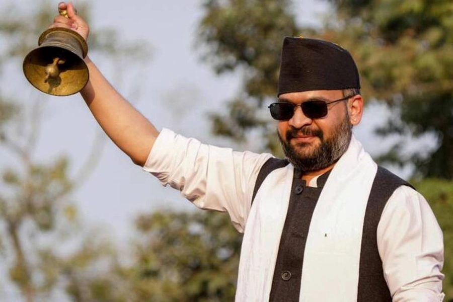 Balen Shah holding a bell, wearing his signature black sunglasses and formal attire, symbolizing leadership and a call for change in Nepal.